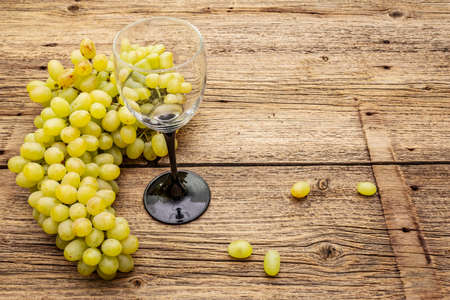 Bunch of sweet green seedless grapes variety "Kishmish". Ripe fruits autumn harvest. Healthy food concept. Old wooden boards background, wine glass, copy spaceの写真素材