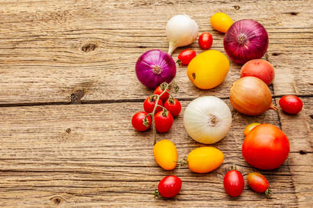 Autumn harvest vegetables cooking background. Assortment of different types onions and tomatoes. Old vintage wooden boards background, copy spaceの写真素材