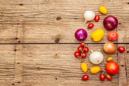 Autumn harvest vegetables cooking background. Assortment of different types onions and tomatoes. Old vintage wooden boards background, copy space, top viewの写真素材