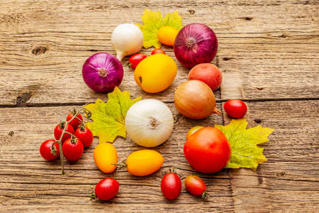 Autumn harvest vegetables cooking background. Assortment of different types onions and tomatoes. Old vintage wooden boards background, close upの写真素材
