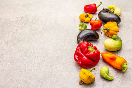 Trendy ugly organic vegetables. Assortment of fresh pepper, eggplant, cucumber, tomato, pumpkin. Cooking ugly food concept. Stone concrete background, copy spaceの写真素材