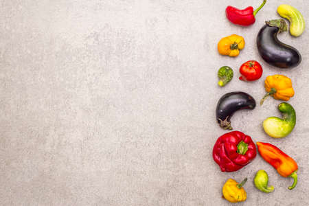 Trendy ugly organic vegetables. Assortment of fresh pepper, eggplant, cucumber, tomato, pumpkin. Cooking ugly food concept. Stone concrete background, copy space, top viewの写真素材