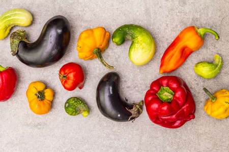 Trendy ugly organic vegetables. Assortment of fresh pepper, eggplant, cucumber, tomato, pumpkin. Cooking ugly food concept. Stone concrete background, top view, close upの写真素材