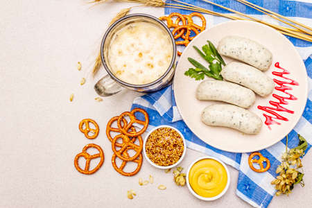 Oktoberfest set. Dark beer, weisswurst, pretzels, mustard, spikelets of grain, hop. Traditional German cuisine, festival food. Mug, linen napkin, stone concrete background copy space top view close upの写真素材