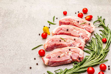 Raw pork belly with rind, peritoneum meat. Fresh tomato cherry, rosemary, spice. Ingredient for cooking healthy meal, animal proteins. Light stone concrete background copy spaceの写真素材