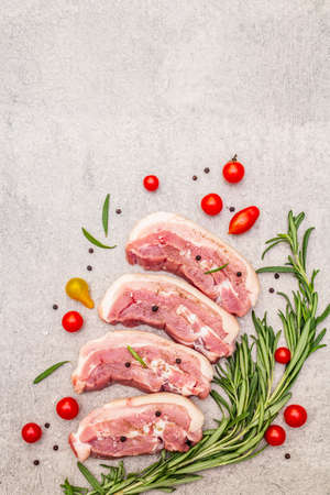 Raw pork belly with rind, peritoneum meat. Fresh tomato cherry, rosemary, spice. Ingredient for cooking healthy meal, animal proteins. Light stone concrete background copy space top viewの写真素材
