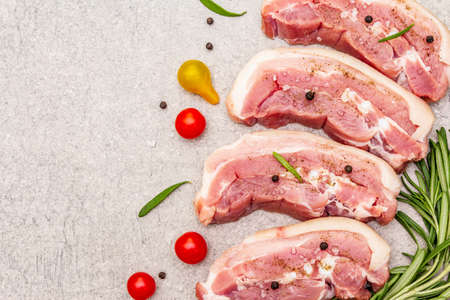 Raw pork belly with rind, peritoneum meat. Fresh tomato cherry, rosemary, spice. Ingredient for cooking healthy meal, animal proteins. Light stone concrete background copy space top viewの写真素材