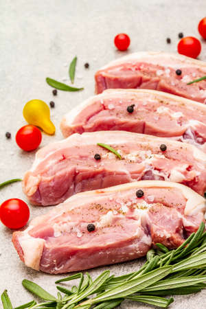 Raw pork belly with rind, peritoneum meat. Fresh tomato cherry, rosemary, spice. Ingredient for cooking healthy meal, animal proteins. Light stone concrete background close upの写真素材