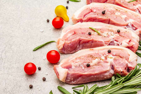 Raw pork belly with rind, peritoneum meat. Fresh tomato cherry, rosemary, spice. Ingredient for cooking healthy meal, animal proteins. Light stone concrete background close upの写真素材