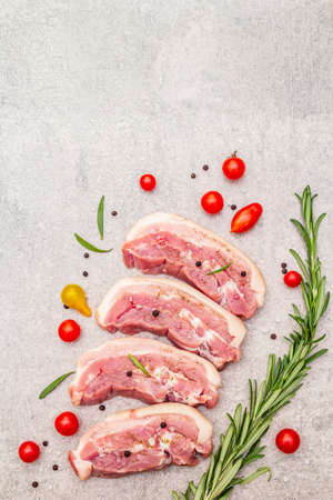 Raw pork belly with rind, peritoneum meat. Fresh tomato cherry, rosemary, spice. Ingredient for cooking healthy meal, animal proteins. Light stone concrete background copy space top viewの写真素材
