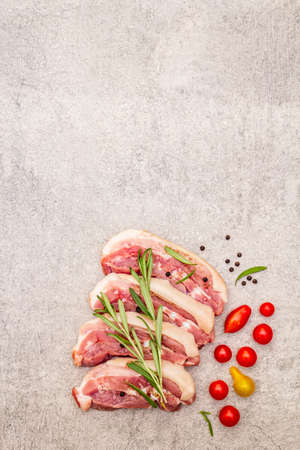 Raw pork belly with rind, peritoneum meat. Fresh tomato cherry, rosemary, spice. Ingredient for cooking healthy meal, animal proteins. Light stone concrete background copy space top viewの写真素材