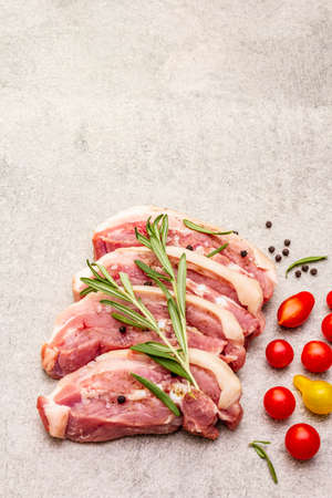 Raw pork belly with rind, peritoneum meat. Fresh tomato cherry, rosemary, spice. Ingredient for cooking healthy meal, animal proteins. Light stone concrete background copy spaceの写真素材