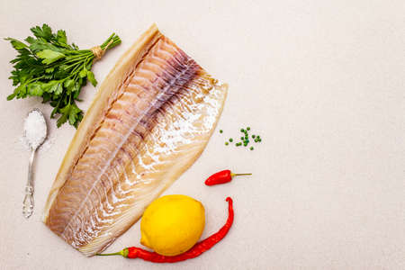 Raw cod loin fillet with lemon, sea salt, chili and cayenne pepper, parsley. Freshly thawed fish, healthy vegetarian food concept. Stone concrete background copy space top viewの写真素材