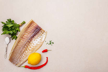 Raw cod loin fillet with lemon, sea salt, chili and cayenne pepper, parsley. Freshly thawed fish, healthy vegetarian food concept. Stone concrete background copy space top viewの写真素材