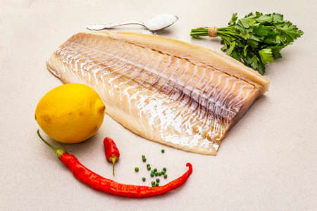 Raw cod loin fillet with lemon, sea salt, chili and cayenne pepper, parsley. Freshly thawed fish,...