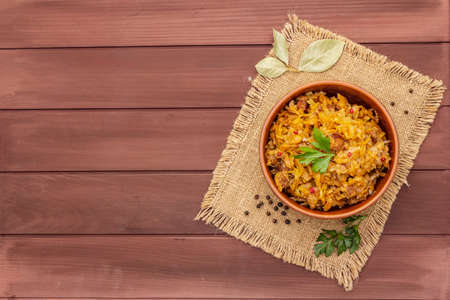 Stewed (braised) cabbage served on ethnic ceramic bowl. Traditional Polish Bigos with meat, aromatic pepper, fresh parsley, vintage sackcloth. Rustic wooden boards background copy space top viewの写真素材