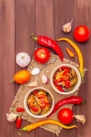 Marinated salad with pickled vegetables: eggplant, carrot, pepper, tomato, garlic. Healthy food concept, autumn harvest products recipe. Wooden boards background, copy space, top viewの写真素材