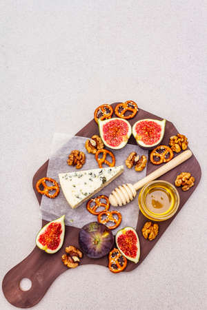 Cheese platter (board) with blue cheese, honey, walnuts, figs, pretzels. Traditional healthy appetizer, snack. Wooden rustic board on stone concrete background, copy space, top viewの写真素材