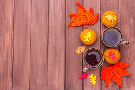 Hot autumn drink. Black tea with cupcakes, colorful leaves. Warm and comfortable mood concept. Wooden boards rustic style background, copy space, top viewの写真素材