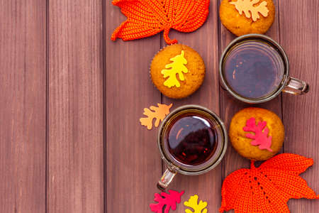 Hot autumn drink. Black tea with cupcakes, colorful leaves. Warm and comfortable mood concept. Wooden boards rustic style background, copy space, top viewの写真素材