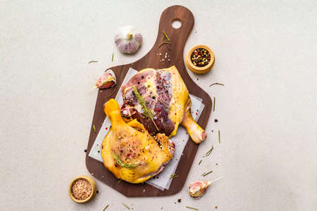 Raw duck legs. Fresh BIO ingredient for preparation traditional French confit. Spice, vegetable, herbs. Animal proteins and healthy fats, wooden board, stone background copy space, top viewの写真素材