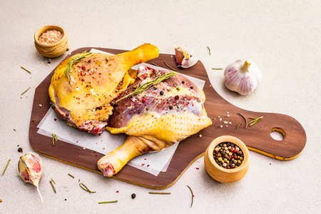 Raw duck legs. Fresh BIO ingredient for preparation traditional French confit. Rosemary, garlic, peppers mix, sea salt. Animal proteins and healthy fats, wooden board, stone background copy spaceの写真素材
