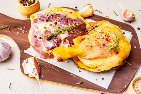 Raw duck legs. Fresh BIO ingredient for preparation traditional French confit. Rosemary, garlic, peppers mix, sea salt. Animal proteins and healthy fats, wooden board, stone background, close upの写真素材