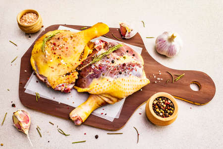 Raw duck legs. Fresh BIO ingredient for preparation traditional French confit. Rosemary, garlic, peppers mix, sea salt. Animal proteins and healthy fats, wooden board, stone background.の写真素材