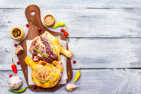 Raw duck legs. Fresh BIO ingredient for preparation traditional French confit. Spice, vegetable, herbs. Animal proteins and healthy fats, cutting board, wooden background copy space, top viewの写真素材