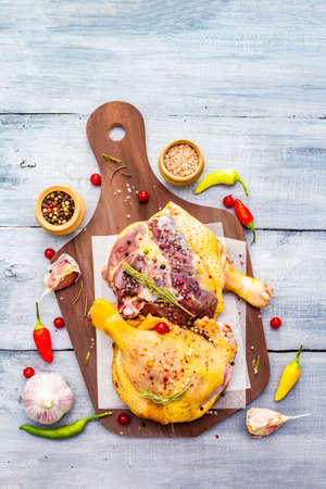 Raw duck legs. Fresh BIO ingredient for preparation traditional French confit. Spice, vegetable, herbs. Animal proteins and healthy fats, cutting board, wooden background copy space, top viewの写真素材