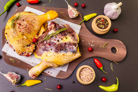 Raw duck legs. Fresh BIO ingredient for preparation traditional French confit. Spice, vegetable, herbs. Animal proteins and healthy fats, wooden board, stone background close upの写真素材
