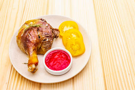 Crusty roasted duck leg. Traditional French food confit preparation. Served with cranberry sauce, fresh tomatoes, dry rosemary. Animal proteins, healthy fats. Wooden background copy space close upの写真素材