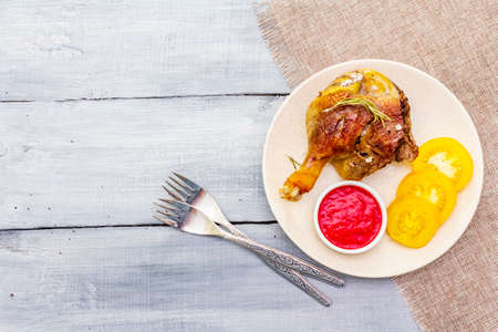 Crusty roasted duck leg. Traditional French food confit preparation. Served with cranberry sauce, fresh tomatoes, dry rosemary. Animal proteins, healthy fats. Wooden background copy space top viewの写真素材