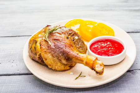 Crusty roasted duck leg. Traditional French food confit preparation. Served with cranberry sauce, fresh tomatoes, dry rosemary. Animal proteins, healthy fats. Wooden background copy space close upの写真素材