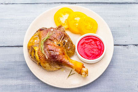Crusty roasted duck leg. Traditional French food confit preparation. Served with cranberry sauce, fresh tomatoes, dry rosemary. Animal proteins, healthy fats. Wooden background copy space top viewの写真素材