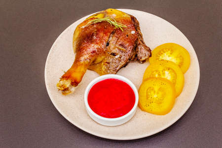 Crusty roasted duck leg. Traditional French food confit preparation. Served with cranberry sauce, fresh tomatoes, dry rosemary. Animal proteins, healthy fats. Stone background close upの写真素材