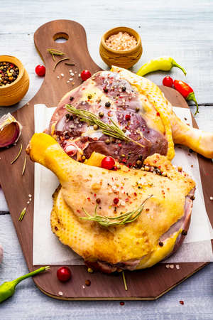 Raw duck legs. Fresh BIO ingredient for preparation traditional French confit. Spice, vegetable, herbs. Animal proteins and healthy fats, cutting board, wooden background, close upの写真素材