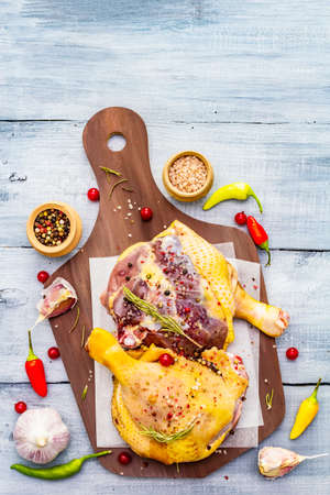 Raw duck legs. Fresh BIO ingredient for preparation traditional French confit. Spice, vegetable, herbs. Animal proteins and healthy fats, cutting board, wooden background copy space, top viewの写真素材