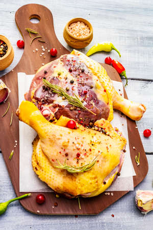 Raw duck legs. Fresh BIO ingredient for preparation traditional French confit. Spice, vegetable, herbs. Animal proteins and healthy fats, cutting board, wooden background, top view, close upの写真素材