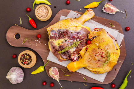 Raw duck legs. Fresh BIO ingredient for preparation traditional French confit. Spice, vegetable, herbs. Animal proteins and healthy fats, wooden board, stone background top view close upの写真素材