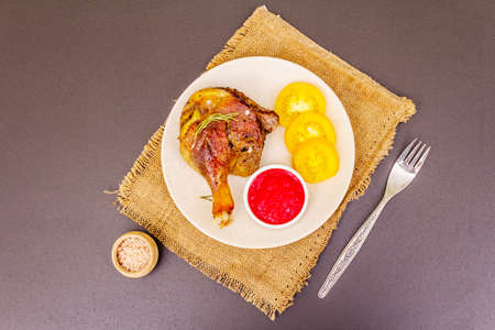 Crusty roasted duck leg. Traditional French food confit preparation. Served with cranberry sauce, fresh tomatoes, dry rosemary. Animal proteins, healthy fats. Stone background copy space top viewの写真素材