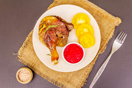Crusty roasted duck leg. Traditional French food confit preparation. Served with cranberry sauce, fresh tomatoes, dry rosemary. Animal proteins, healthy fats. Stone background copy space top viewの写真素材