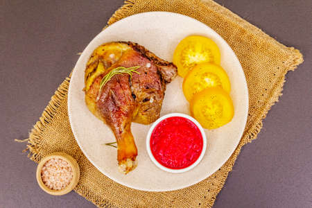 Crusty roasted duck leg. Traditional French food confit preparation. Served with cranberry sauce, fresh tomatoes, dry rosemary. Animal proteins, healthy fats. Stone background top view close upの写真素材