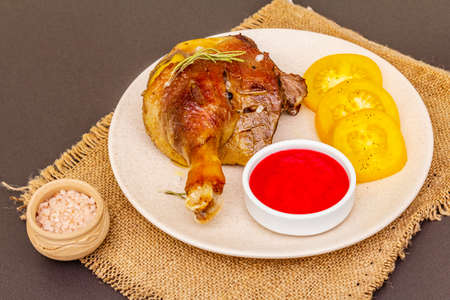 Crusty roasted duck leg. Traditional French food confit preparation. Served with cranberry sauce, fresh tomatoes, dry rosemary. Animal proteins, healthy fats. Stone background close upの写真素材