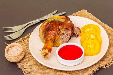 Crusty roasted duck leg. Traditional French food confit preparation. Served with cranberry sauce, fresh tomatoes, dry rosemary. Animal proteins, healthy fats. Stone background close upの写真素材