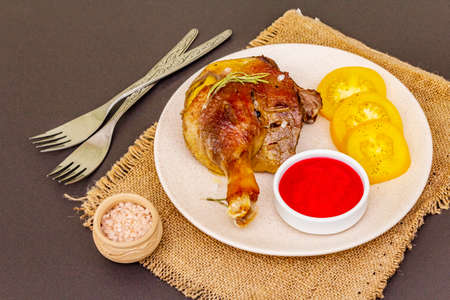 Crusty roasted duck leg. Traditional French food confit preparation. Served with cranberry sauce, fresh tomatoes, dry rosemary. Animal proteins, healthy fats. Stone backgroundの写真素材