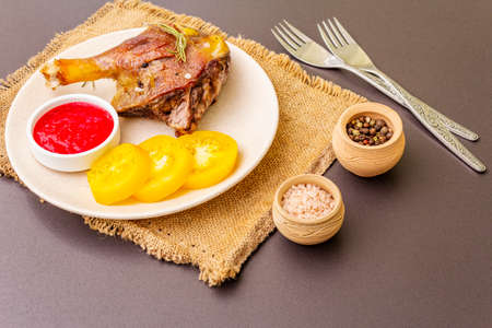 Crusty roasted duck leg. Traditional French food confit preparation. Served with cranberry sauce, fresh tomatoes, dry rosemary. Animal proteins, healthy fats. Stone background copy spaceの写真素材
