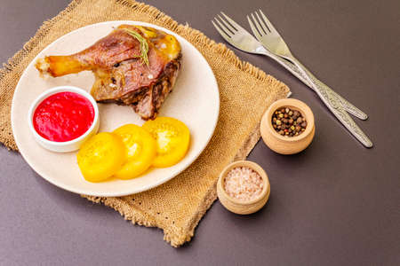 Crusty roasted duck leg. Traditional French food confit preparation. Served with cranberry sauce, fresh tomatoes, dry rosemary. Animal proteins, healthy fats. Stone background copy spaceの写真素材