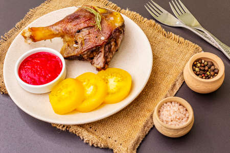 Crusty roasted duck leg. Traditional French food confit preparation. Served with cranberry sauce, fresh tomatoes, dry rosemary. Animal proteins, healthy fats. Stone background close upの写真素材