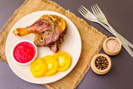 Crusty roasted duck leg. Traditional French food confit preparation. Served with cranberry sauce, fresh tomatoes, dry rosemary. Animal proteins, healthy fats. Stone background close upの写真素材